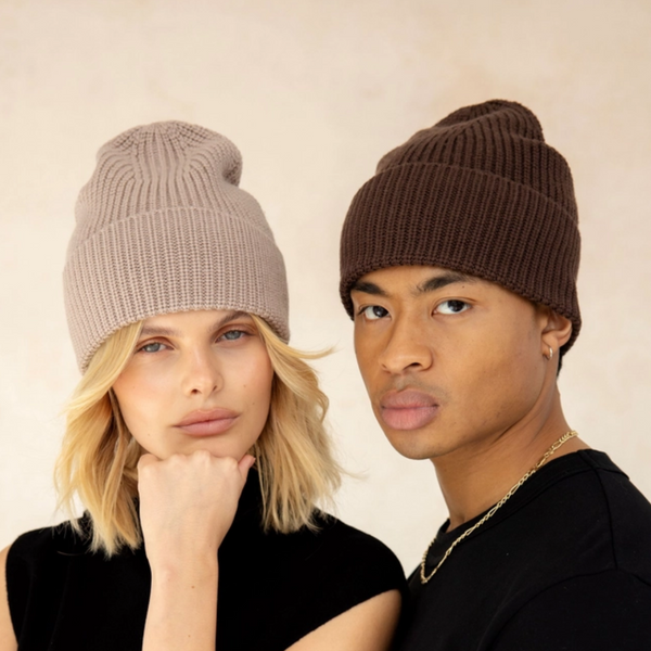 Two people wearing beige and brown knit hats against a plain background