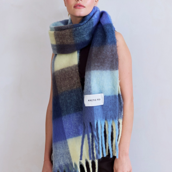 Person wearing a blue and yellow checkered scarf with a visible brand label on a plain background