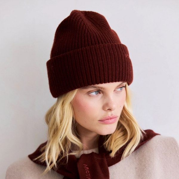 Woman wearing a brown knit beanie and scarf against a light background