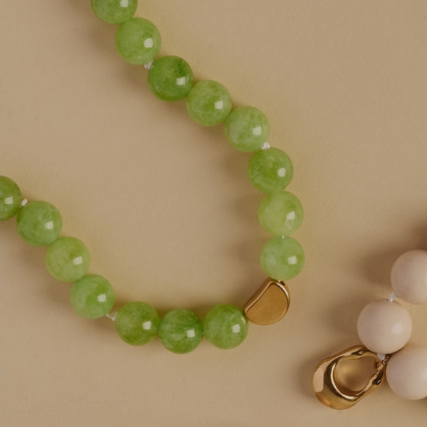 Green beaded necklace with a gold charm on a beige background