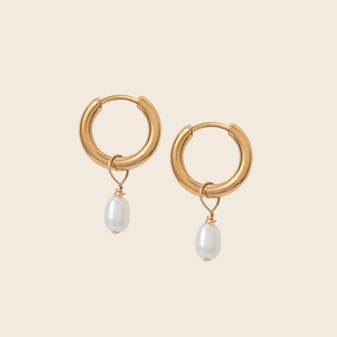Gold hoop earrings with pearl drops on a beige background