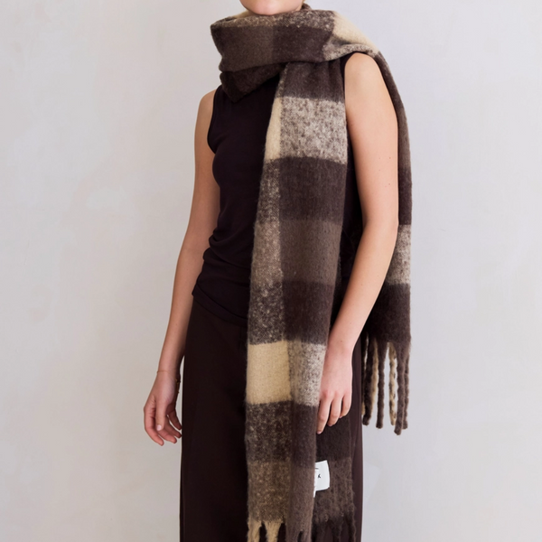 Person wearing a plaid scarf with brown, beige, and black colors on a plain background