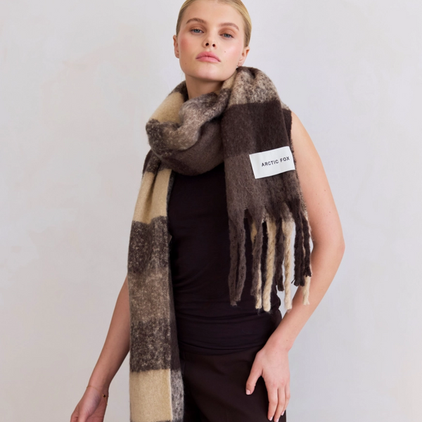 Woman wearing a plaid brown, beige and black scarf with a visible brand label on a plain background