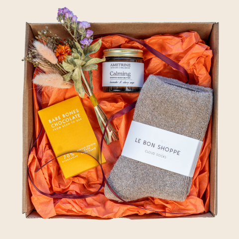 Gift box with a candle, chocolate bar, and socks on orange tissue paper.