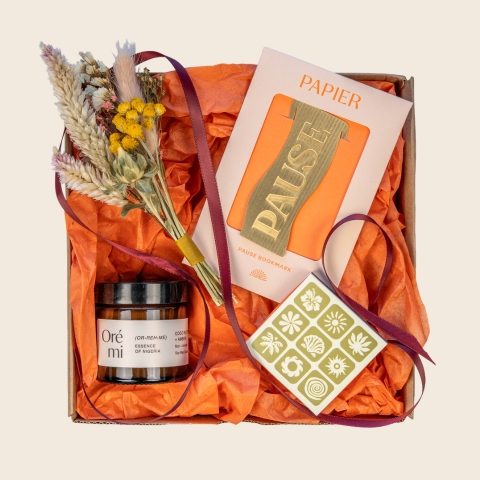 Gift box with a candle, dried flowers, and a bookmark titled 'Pause' on an orange tissue background.