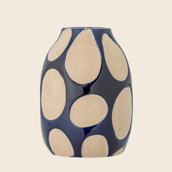 A glossy ceramic vase with a dark navy blue base and large, irregular beige polka dots, shown against a solid light beige background.
