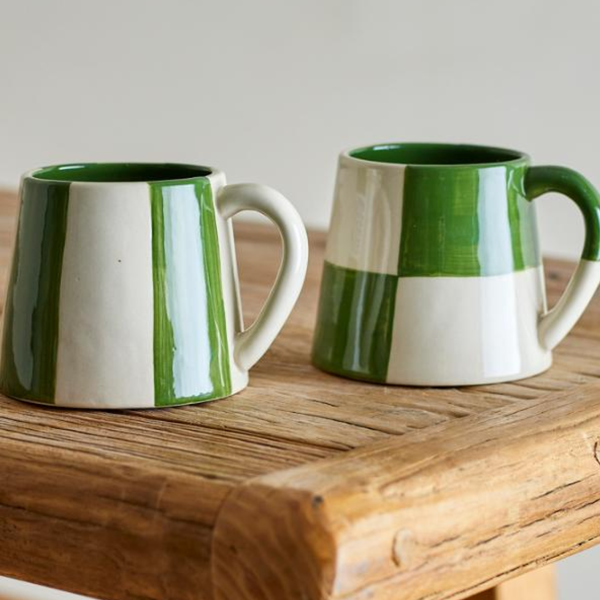 Two green and white ceramic mugs with a rustic wooden table background.