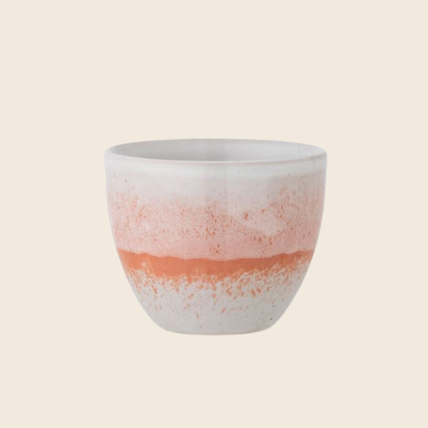 A small handmade ceramic cup with a white and orange mix pattern set against a solid cream background.
