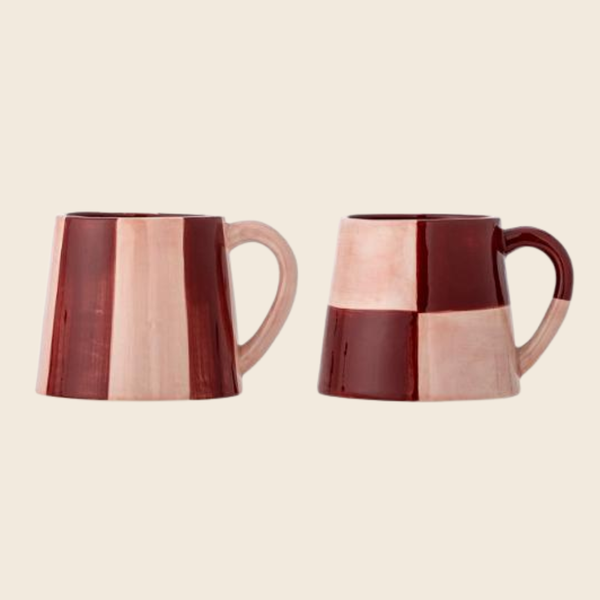 Two ceramic mugs with a glossy checkered and stripe pattern in deep burgundy and light pink, shown from different angles on a solid cream background.