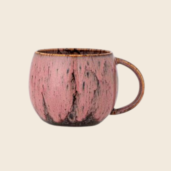 A handmade ceramic mug with a textured pink and dark brown glaze, featuring a rustic finish and a curved handle, set against a solid light beige background.