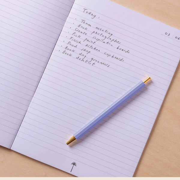 A light blue pencil with gold metal ends rests on an open lined notebook with handwritten notes, placed on a light wood surface.