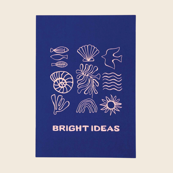A vertical rectangular notebook with a deep blue background, featuring white line drawings of sea life and marine motifs, including fish, a shell, a bird, a spiral shell, seaweed, waves, a coral-like shape, a rainbow, a sun, and the words “BRIGHT IDEAS” at the bottom. The item is centered on a light warm beige background.