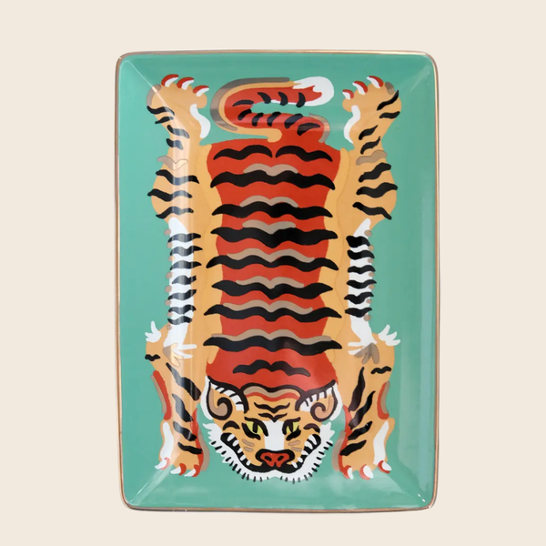 A rectangular ceramic trinket dish featuring a stylised tiger illustration on a turquoise background, photographed against a light beige backdrop.