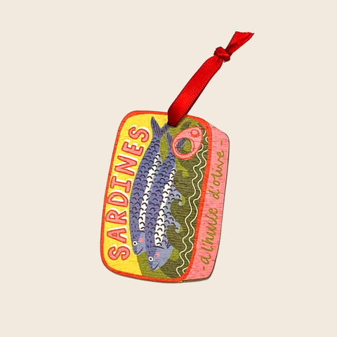 Colorful sardine can-shaped ornament with a red ribbon on a beige background
