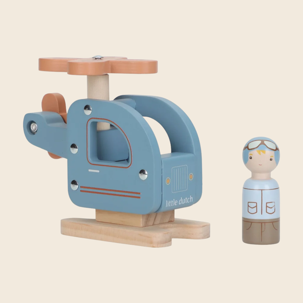 A wooden toy helicopter with a light blue body, natural wood base and rotor, shown next to a small wooden pilot figure on a plain beige background. The toy has the text 'little dutch' printed on the side.