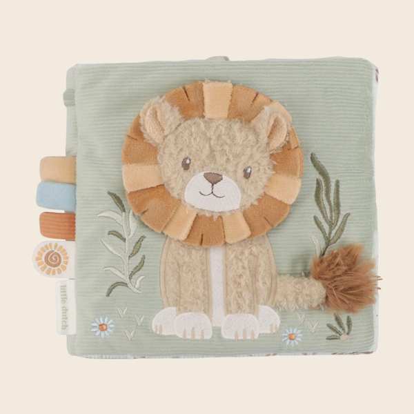 A square baby activity book or soft toy made of pale sage green corduroy fabric, featuring an embroidered lion face and mane on the front, with small leaf and flower details and tabbed edges on the left.