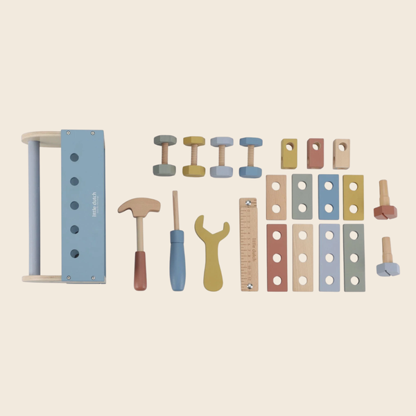 A wooden toy workshop set laid out on a light beige background, including a blue and wood frame, small dumbbells, pegs, a hammer, a screwdriver, a wrench, a ruler, and colored wooden blocks.