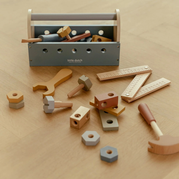 Little Dutch wooden toy toolbox set with assorted tools including a hammer, wrench, screw, nuts, bolts, and rulers, arranged on a light wood surface.