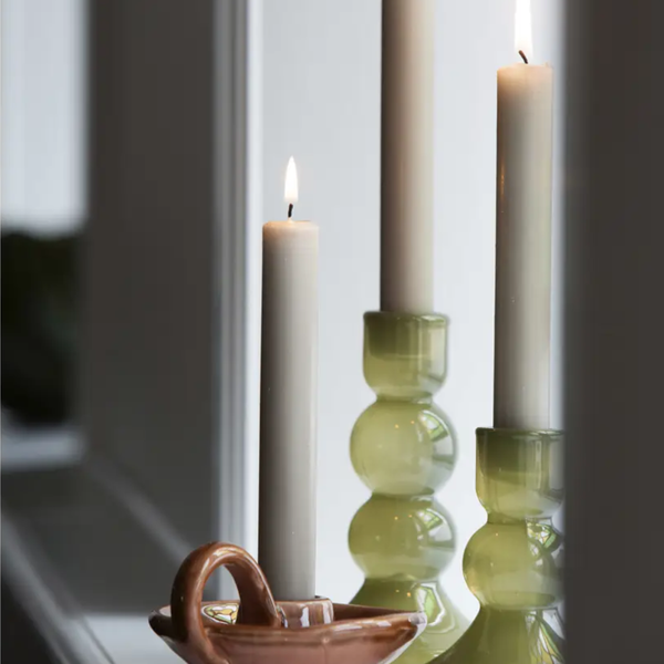 Three lit taper candles in glass candlesticks and a small ceramic holder, arranged near a window with soft natural light.
