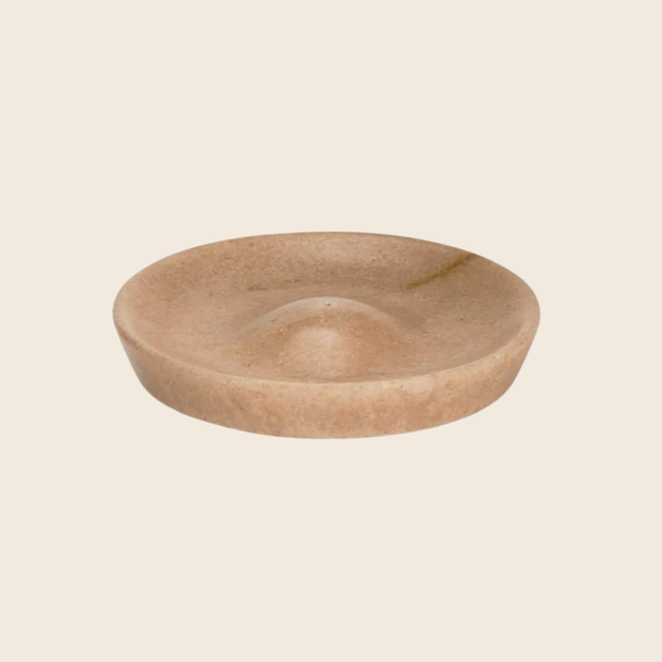 A round, shallow marble incense dish with a textured, organic surface in a warm sandy beige colour, shown against a solid cream background.