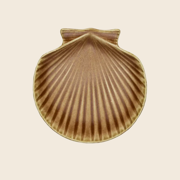 A scallop shell-shaped ceramic plate or dish with a ribbed texture, featuring a warm brown and beige colour palette, centred on a solid light beige background.