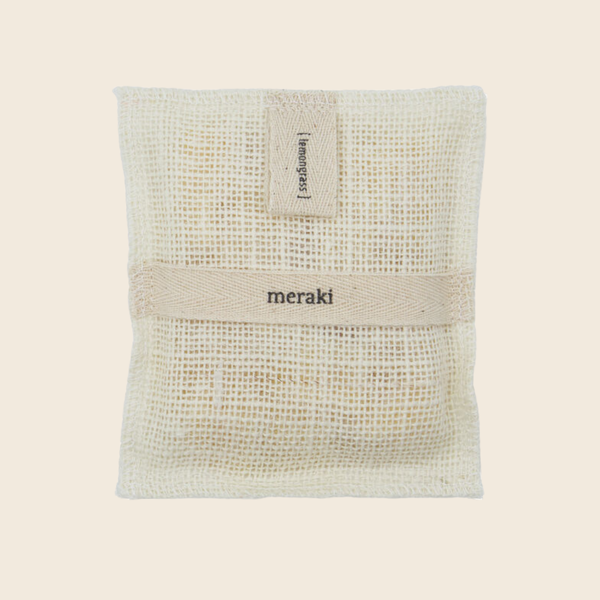A square natural bath mitt with a beige  band across the middle and a small fabric 'lemongrass' tag at the top, printed with the brand name 'meraki'.