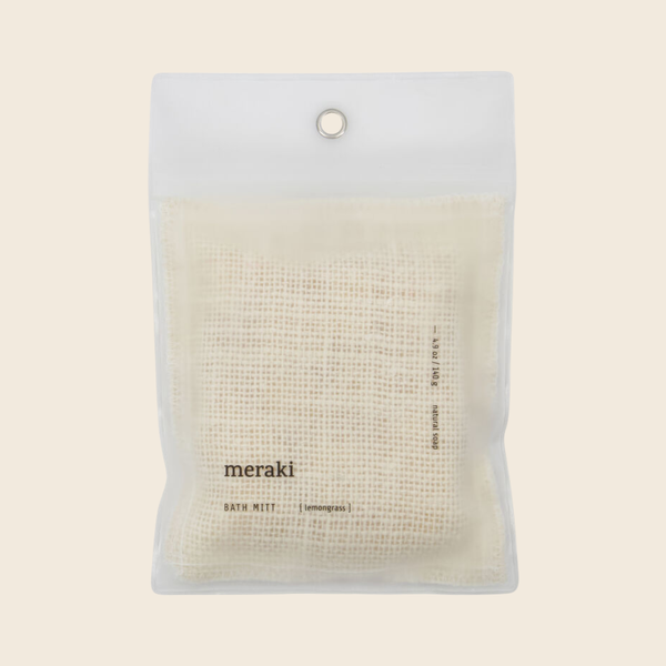 A packaged bath mitt from the brand meraki, shown in a clear plastic hanging pouch against a solid light beige background.