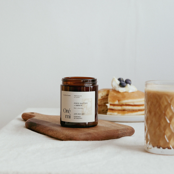 Candle labeled 'Ore mi' on a wooden board with pancakes and coffee in the background