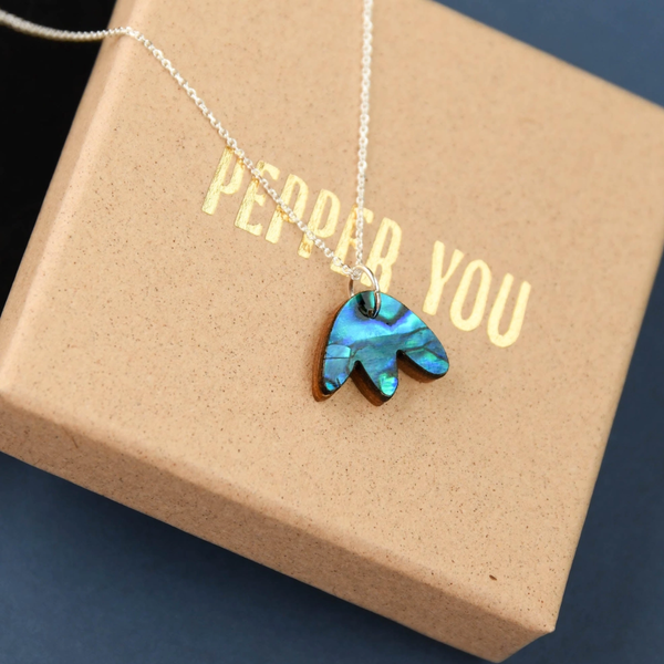 A silver necklace with a small pendant made of iridescent blue-green abalone shell, displayed on a brown gift box printed with the words 'PEPPER YOU'.