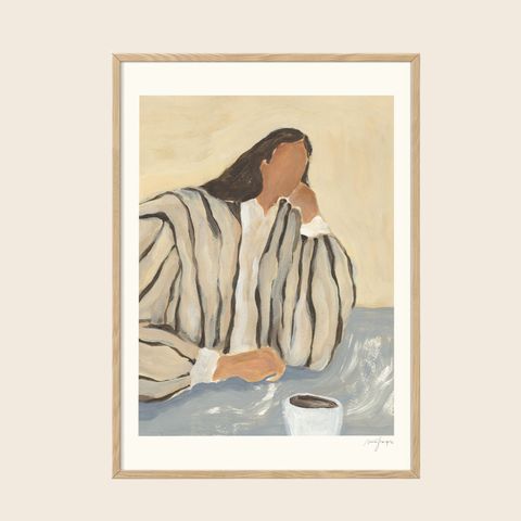 Framed artwork of a person in a robe with a cup on a table, on a beige wall.