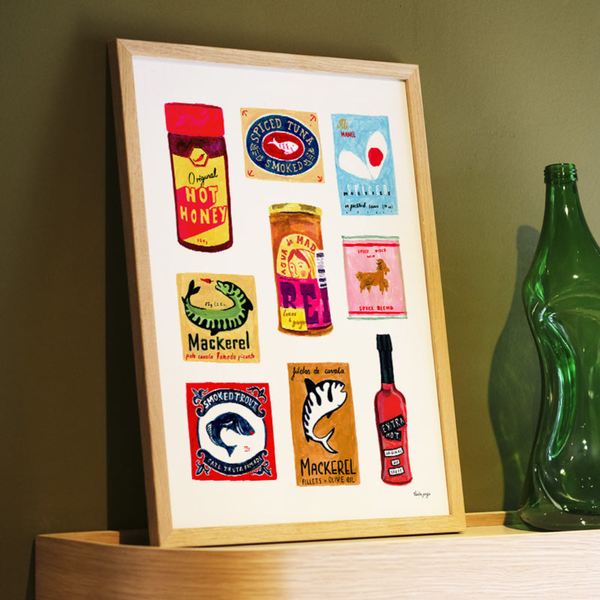 Framed artwork with colorful labels on a shelf next to a green bottle.
