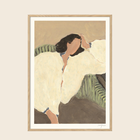 Framed artwork of a woman sitting on a couch with a white blanket, on a beige wall.