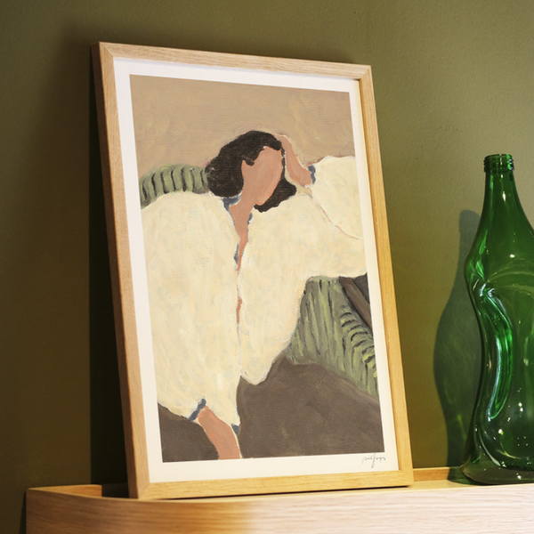 Framed artwork of a woman in a white coat on a wooden shelf with a green bottle.