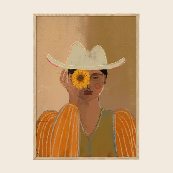 A framed art print featuring a stylised portrait of a woman wearing a white cowboy hat and an orange striped top, with a yellow flower covering one of her eyes, set against a warm beige background.