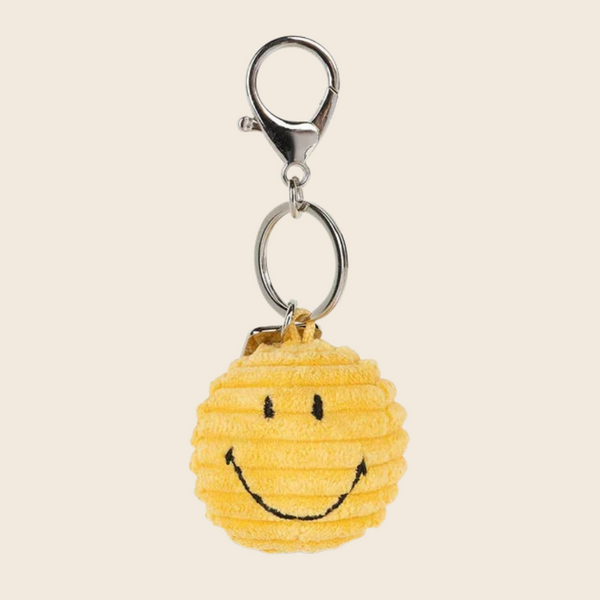A yellow corduroy textured smiley face keychain charm with a silver lobster clasp and key ring, shown against a solid light beige background.