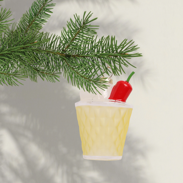 Decorative ornament shaped like a cocktail with a red chilli pepper on top, hanging from a Christmas tree branch.