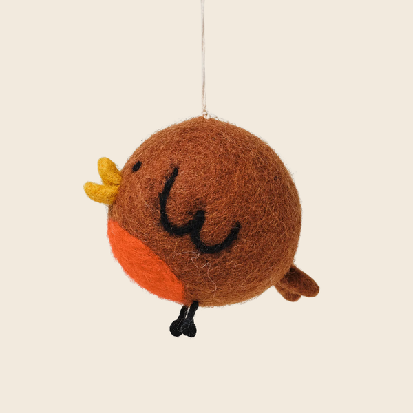 A cute, hand-felted bird ornament hanging from a thin string. The ornament features a brown body, a bright orange belly, a small yellow beak, and black embroidered facial features and legs, set against a solid light beige background.
